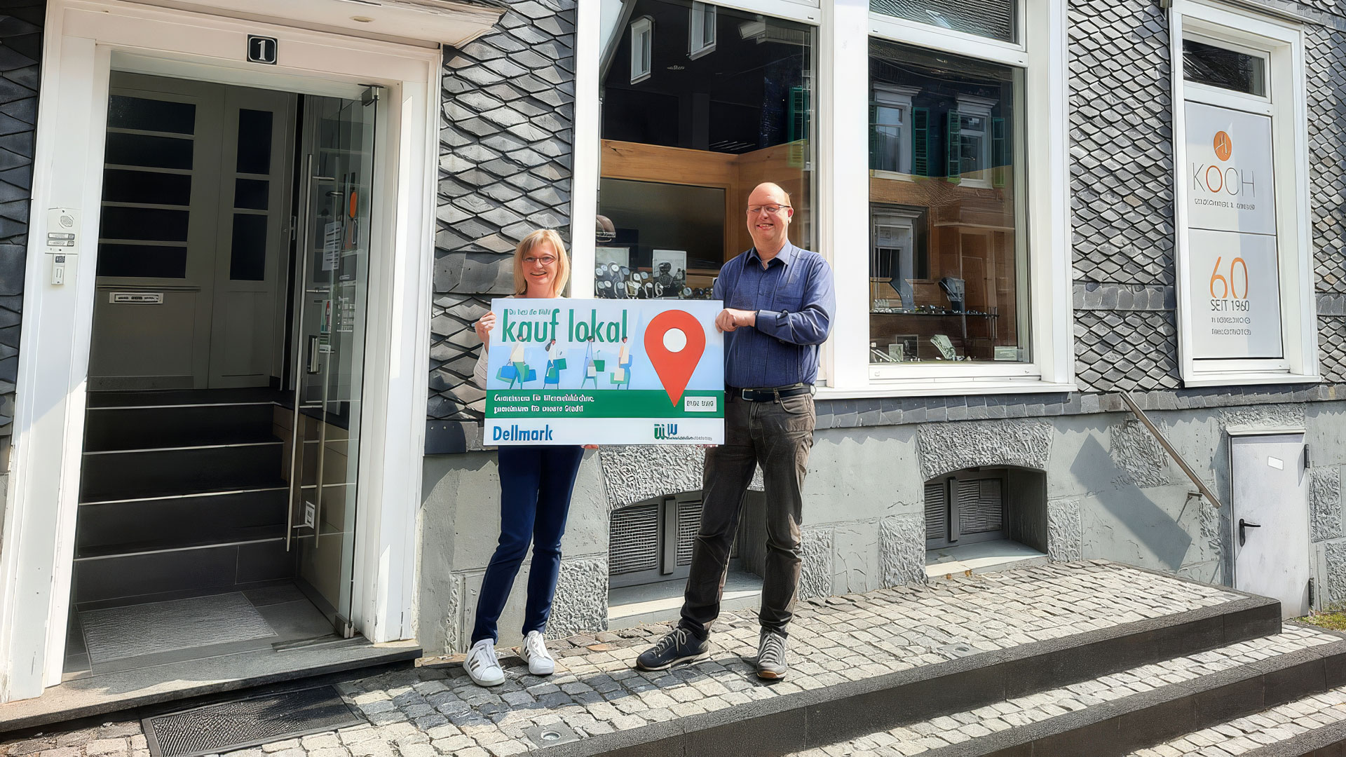 Zwei Personen mit Schild „kauf lokal“ vor einem Geschäftseingang
