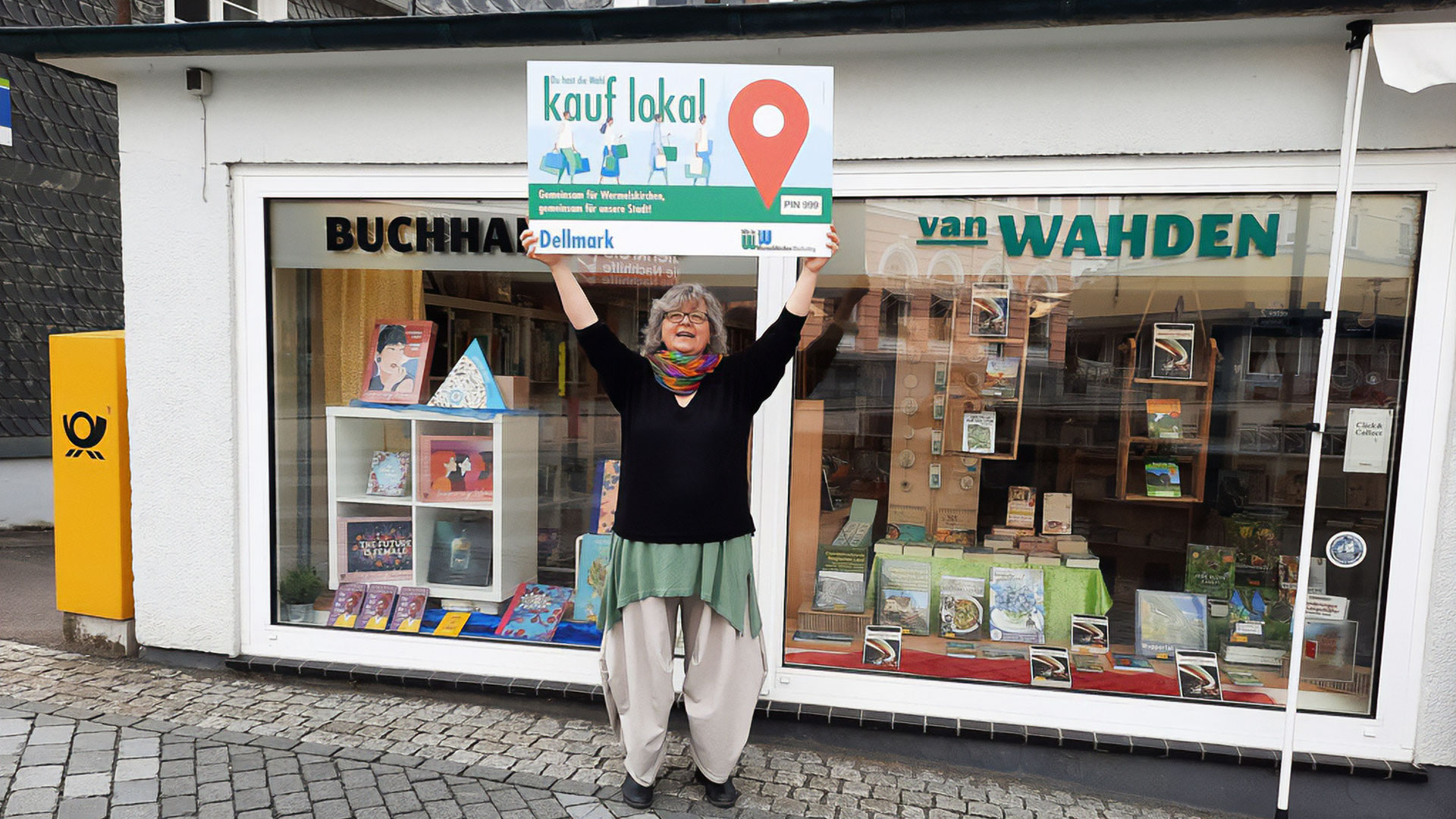 Frau mit Schild „kauf lokal“ vor der Buchhandlung van Wahden