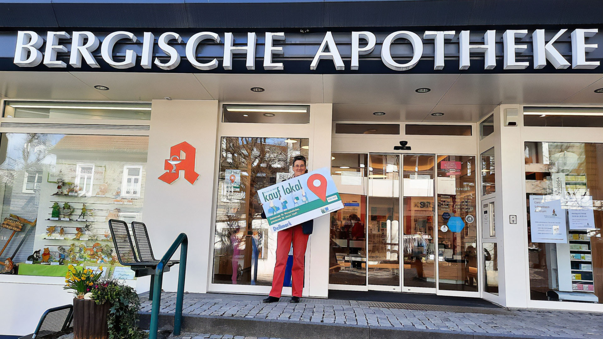 Mitarbeiterin mit Schild „kauf lokal“ vor der Bergischen Apotheke
