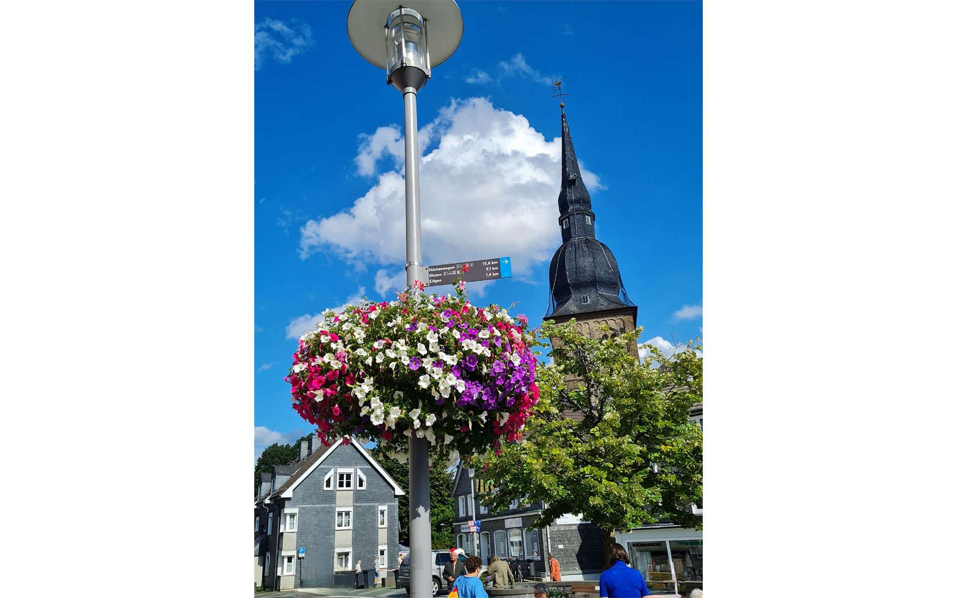 Blumenampel an einer Laterne, im Hintergrund ein Kirchturm