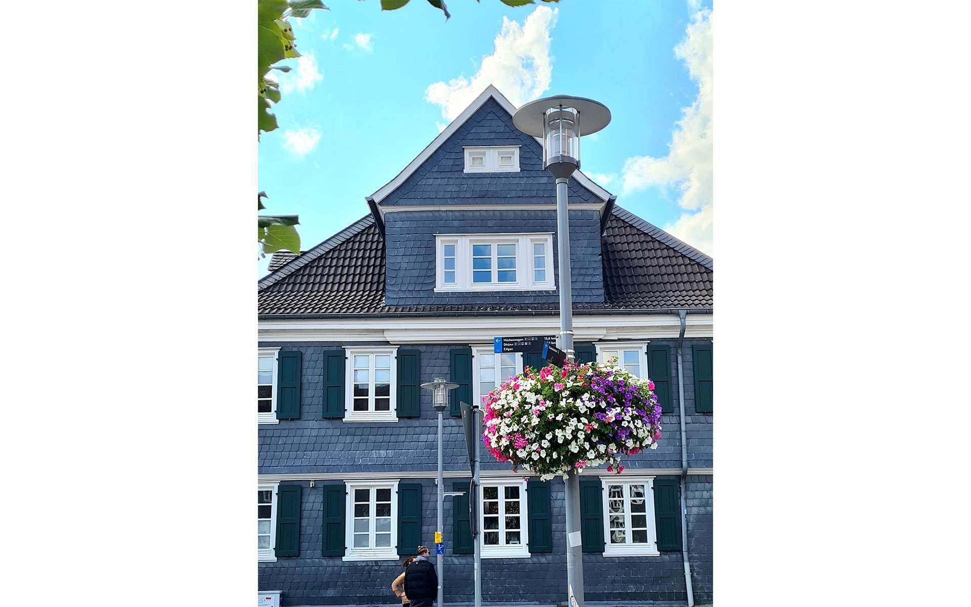 Blumenampel vor einem Schieferhaus mit grünen Fensterläden