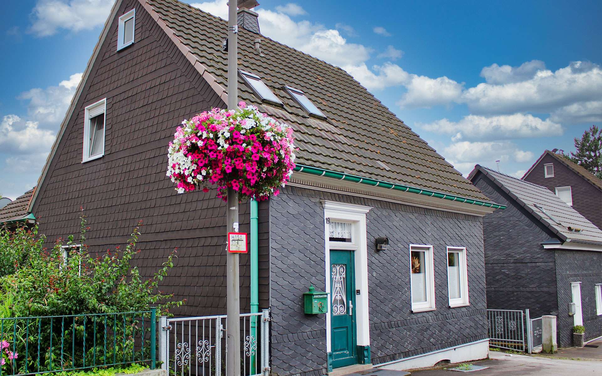 Blumenampel an einer Laterne vor einem Schieferhaus