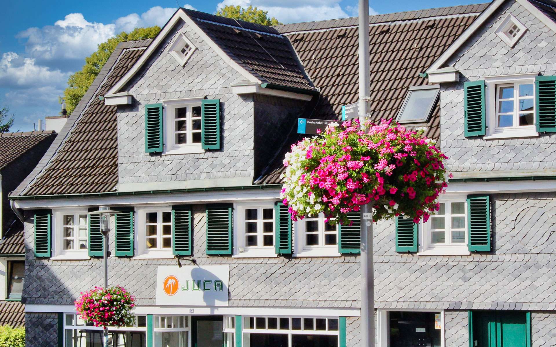 Blumenampel vor einem Schieferhaus mit grünen Fensterläden