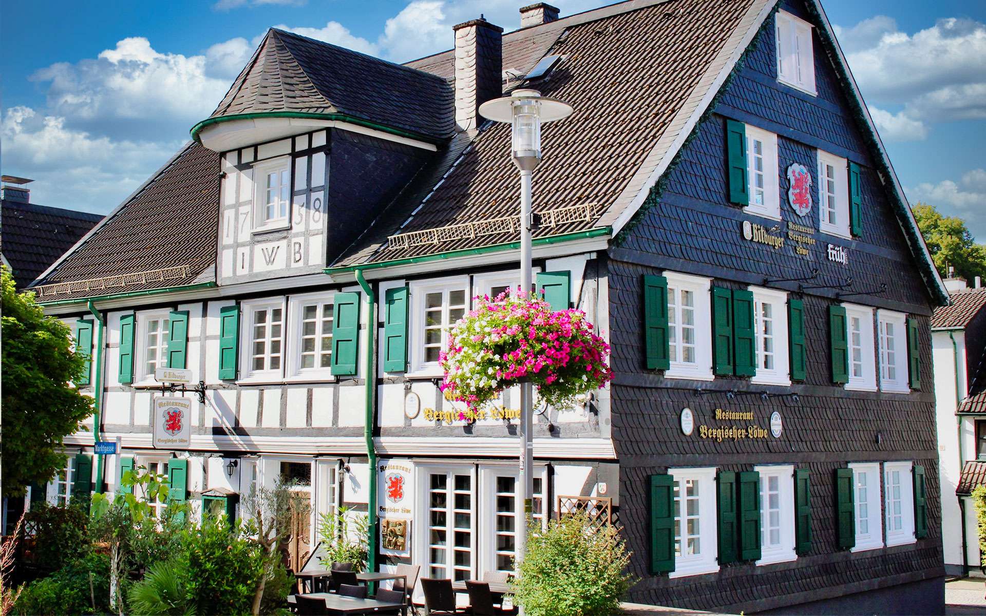 Blumenampel vor einem bergischen Fachwerkhaus mit grünen Fensterläden