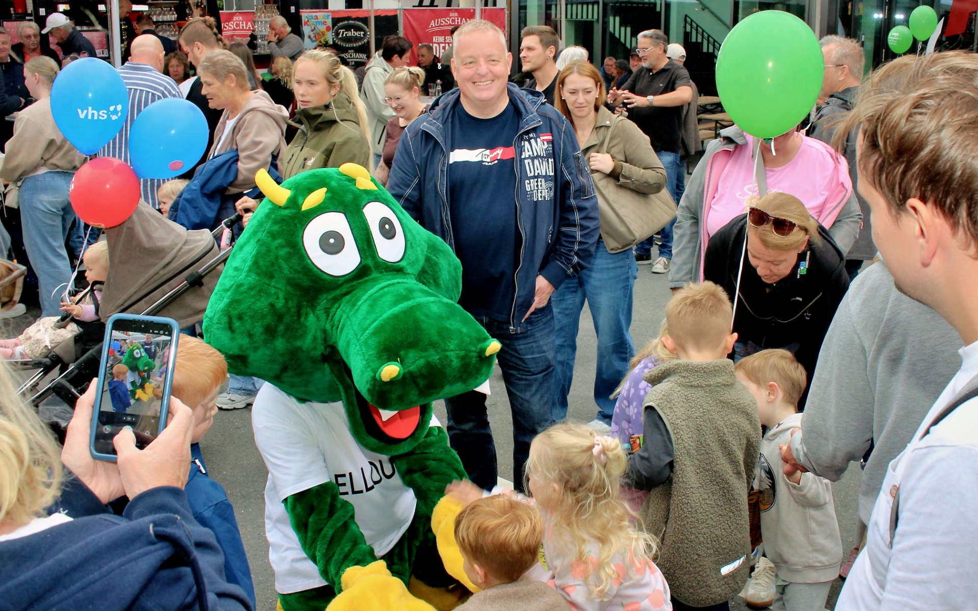 Maskottchen Dellouga zwischen Besuchern mit Luftballons am Kirmessonntag